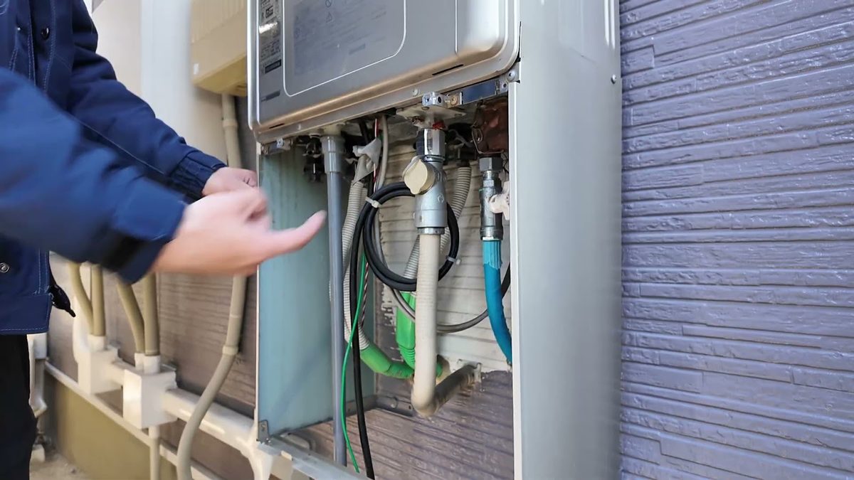 屋外の給湯器の下部で、給排水管・ガス管・電線を当社スタッフが指し示している様子