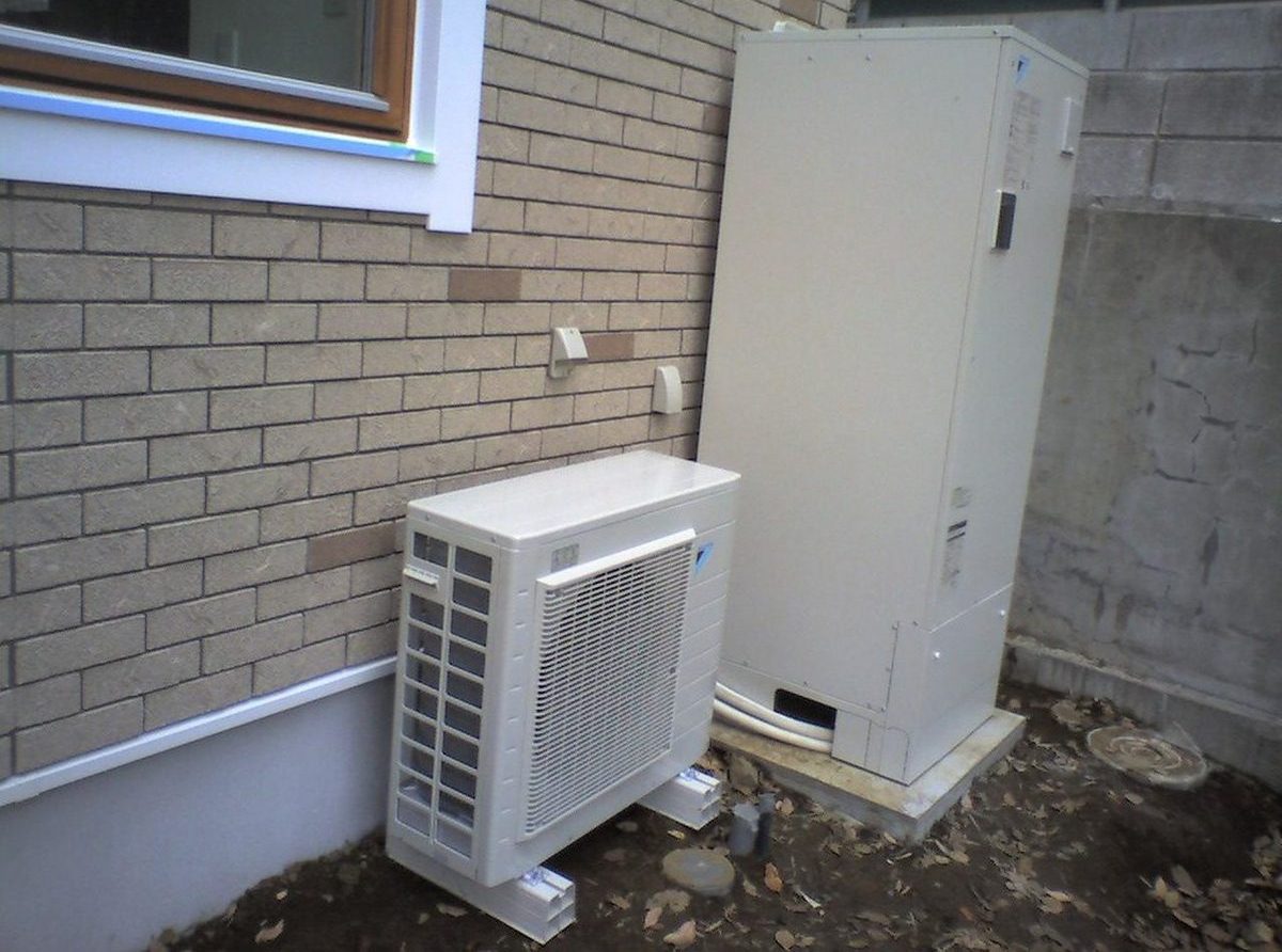 住宅の外壁沿いに設置されたエコキュート一式。手前に四角いヒートポンプユニット、奥に背の高い貯湯タンクユニットが並んでいる