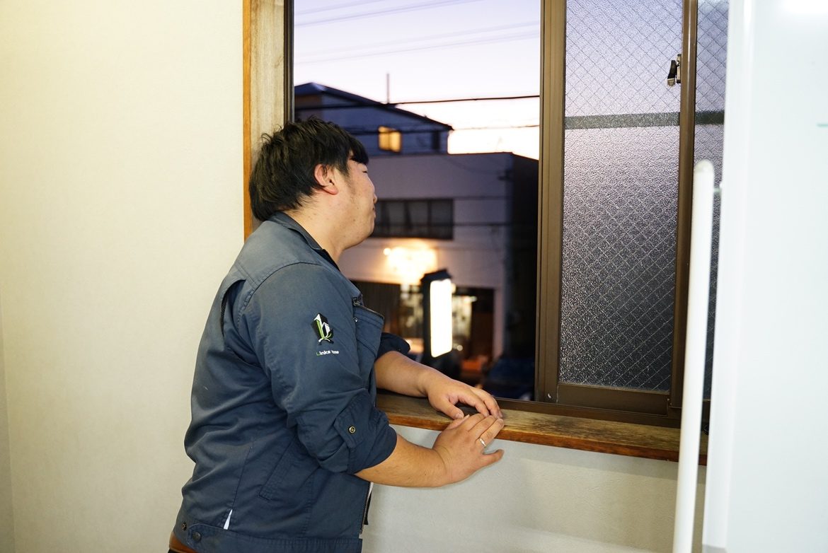 作業着の社員が室内側から窓枠に手を添えて、建具の状態を確認している様子